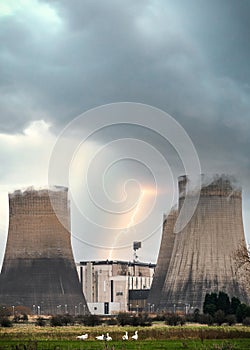 Flash bolt of lightning striking electric power station with cooling tower steam chimneys in storm with dramatic stormy clouds