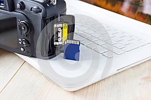 Flash card in hand on camera and laptop background, memory card for SLR camera, flash drive, photo storage