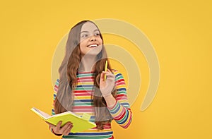 Flash of genius. Happy girl hold copybook pointing pen up. Child genius yellow background