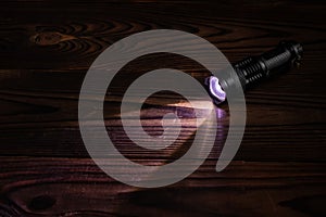 Flashlight and a beam of light in darkness. A modern led lamp with bright projection on dark wood table