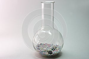 Flat-bottomed round flask with high narrow neck, of borosilicate glass filled with colorful pills