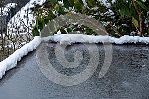 Flat carport roof covered in snow, slush, ice, and water, with clogged downspout drain