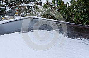 Flat carport roof covered in snow, slush, ice, and water, with clogged downspout drain, residential neighborhood