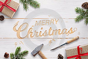 Flat Christmas greeting with carved text into white wooden surface with chisel and hammer