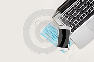 Flat composition of black and white laptop keyboard, phone, coffee cup and blue medical mask on wooden table background. Top view