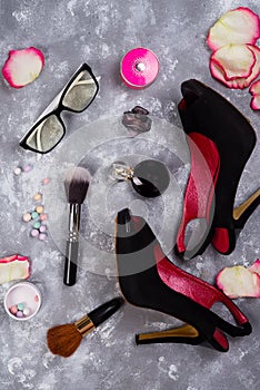 Still life of fashion woman. Women`s fashion with petals of roses, cosmetics, glasses and shoes on stone background, photo