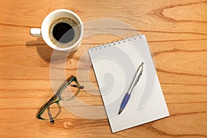 Flat desk, top view office table. Workspace with notepad, pencil, green frame glasses and coffee cup on wooden background.