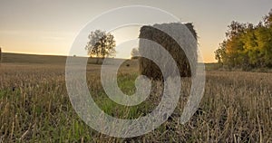 Flat hill meadow timelapse at the summer sunrise time. Wild nature and rural haystacks on grass field. Sun rays and