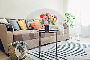 Flat interior of living room decorated with bouquet of peonies, basket, plants and carpet. Cat sleeping on couch