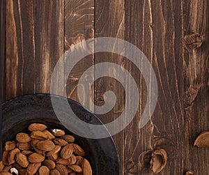 Flat lay of almonds in black plate with other accessories on brown wooden background top view 3