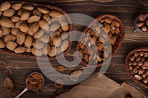 Flat lay of almonds in the wicker plates with other accessories on brown wooden background top view