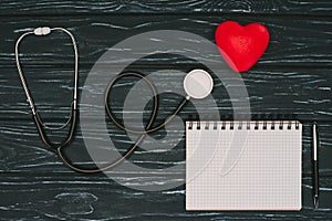 flat lay with arranged red heart, stethoscope and empty notebook on dark wooden tabletop, world health