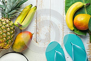 Flat Lay Arrangement Composition Tropical Fruits Pineapple Mango Bananas Green Palm Leaf Women Hat Blue Slippers on White Wood