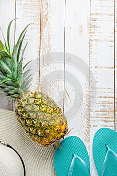 Flat Lay Arrangement Composition with Tropical Fruits Pineapple Women Hat Blue Slippers on White Planked Wood Background. Vacation