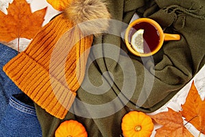 Flat lay autumn composition with fall leaves, pumpkins, hot cup of tea and a warm woolen scarf and hat