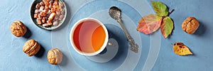 A flat lay autumn panorama with a cup of tea, nuts, and fall leaves, shot from above