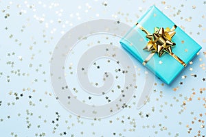 Flat lay background for celebration Christmas and New Year. Gift box turquoise with gold ribbons bows and confetti stars on a blue
