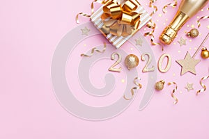 Flat lay background for Christmas and New Year. Champagne bottle, golden gift or present box, 2020 number and confetti on pink