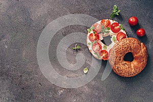 Flat lay bagel sandwich with cream cheese, cherry tomatoes and basil sprinkled with sesame and flax seeds, dark rustic background