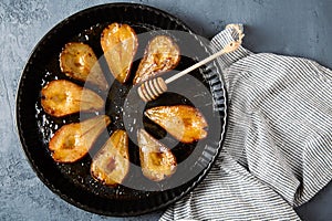 Flat lay of baked pears with honey in a round black tray on a grayish blue background