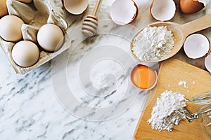 Flat lay of baking ingredients with eggs and flour on marble table