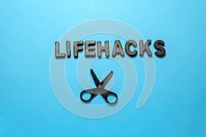 flat lay black letters inscription lifehacks and scissors on a blue background