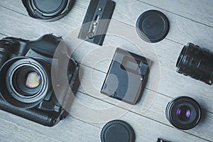 Flat lay with black photoaccessories on white boards: camera, lenses, battery, charger, synchronizer, and lens covers