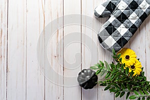 Flat lay with a black and white oven mitt, sunflowers, leaves and a black pumpkin on a light wood panel background, usefull for