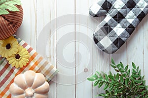 Flat lay with a black and white oven mitt, sunflowers, leaves and a black pumpkin on a light wood panel background, usefull for