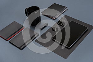 Flat lay of blank black paper sheet, black stationery items and coffee cup on gray desktop. Mock up