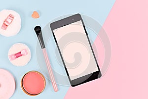 Flat lay with blank black smart phone with empty screen next to cute rouge and brush bauty products