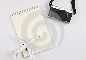 flat lay of blank page opened notebook, airplane model and camera on white background with copy space. Travel, photo and memory