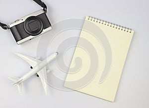 flat lay of blank page opened notebook, airplane model and camera on white background with copy space. Travel, photo and memory