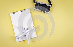 flat lay of blank page opened notebook, airplane model and camera on yellow background with copy space. Travel, photo and memory