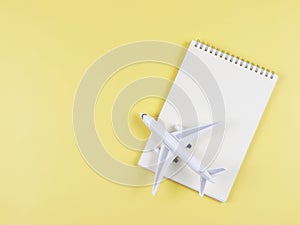 flat lay of blank page opened notebook, airplane model on yellow background with copy space. Travel planning concept