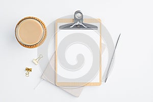 Flat lay blank paper clipboard, cup of coffee and office supplies on white table. Top view minimalist style feminine workspace,