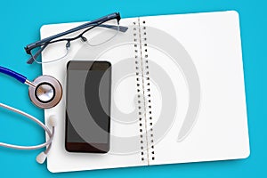Flat lay of blue stethoscope, glasses and mobile smart phone on