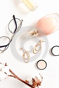 Flat lay of bottles of perfume, golden earrings, glasses and cotton branch