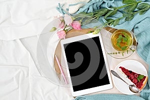 Flat lay breakfast in bed with raspberry cheesecake, mint tea and open note book, tablet