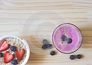 Flat lay of  breakfast with a  glass of blueberry smoothie and oat or granola in white bowl, fresh blueberries, strawberries on