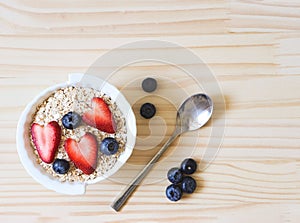 Flat lay  of breakfast with oat or granola in white bowl, fresh blueberries, strawberries  on wooden table. Healthy breakfast