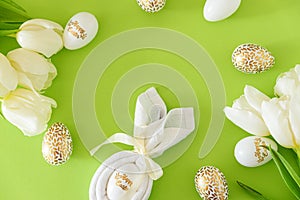Flat lay with bunny ears napkin, white tulips and Easter eggs on green background. Easter celebration concept. Top view