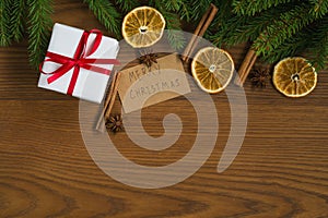 Flat lay christmas background with spruce twigs and white gift box with red ribbon on ash wood surface