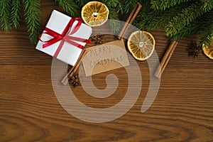 Flat lay christmas background with spruce twigs and white gift box with red ribbon on ash wood surface