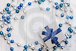 Flat lay Christmas gift with blue ribbon and silver and blue Christmas balls and garland on white wooden background