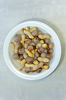 Flat lay, close-up of assorted nuts: hazelnuts, peanuts, brazil nuts (macadamia) in a white plate.