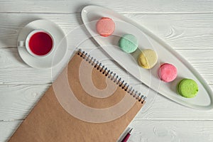 Flat lay. Close up. Provence breakfast. Bright colorful macarons, brown vintage notebook, a pen, a cup of berry tea. Copy space