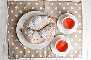 Flat lay, close up. Romantic breakfast for two. Freshly baked French croissants and berry tea. One of the croissants is cut.