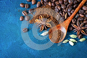 Flat lay. Coffee grains scattered on a blue textural background, anise stars, cardamom and ground coffee in a wooden spoon. Top