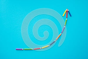 Flat lay of color pencils curve graph growth up form on blue background with copy space. Business growth, creative idea, kids art